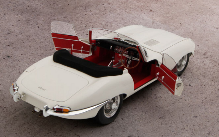 White classic Jaguar convertible sports car with both doors open, revealing a red interior and wooden steering wheel, parked on a gravel surface. The car is vintage, emphasising the appeal of used cars alongside new cars.