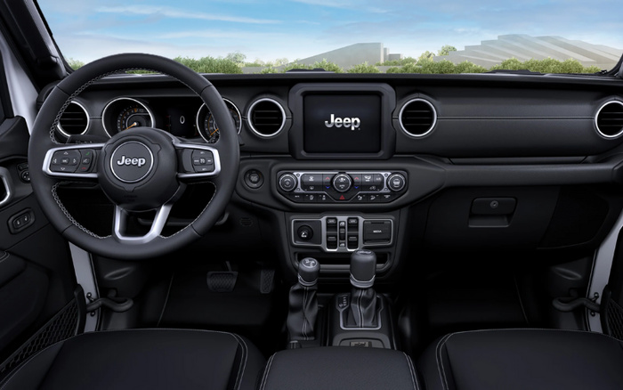 Interior view of a Jeep vehicle showcasing the steering wheel with Jeep logo, dashboard with circular air vents, central touchscreen displaying the Jeep logo, various control buttons and dials for climate and media settings, gear shifters, and black leather seats, representing features found in new cars available alongside used cars.