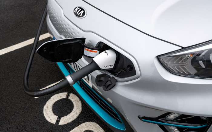 White Kia electric car being charged with an IONITY charger at a charging station, focusing on the charging port and cable connected to the front of the vehicle, suitable for new cars and used cars.