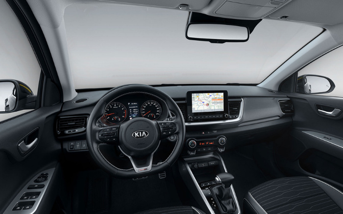 Interior view of a modern Kia car showcasing the steering wheel with Kia logo, dashboard, digital display with navigation system, air conditioning controls, gear shift, and fabric seats. This image highlights the clean and functional design ideal for customers interested in used cars or new cars.