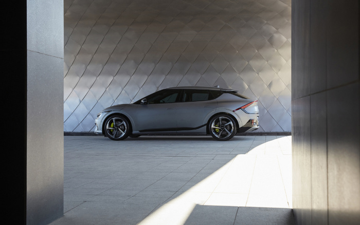 Side view of a modern silver electric car parked in a sleek, contemporary setting with a diamond pattern metallic wall background, showcasing a clean and futuristic design. Ideal image for used cars and new cars advertisements.