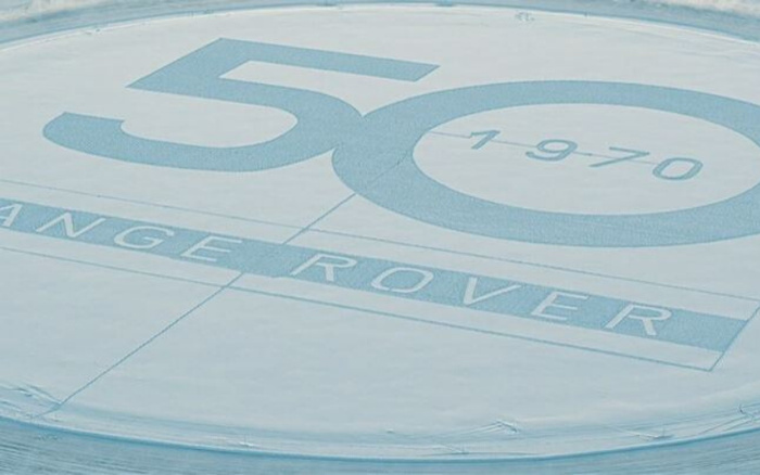 Close-up of a printed or painted surface displaying a large '50' with the year '1970' inside a circle next to it, and the word 'Range Rover' beneath, symbolising 50 years of Range Rover vehicles, relevant to used cars and new cars celebrations.