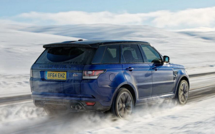 Blue Range Rover Sport driving on a snowy landscape, rear view showing the UK license plate VF64 EHZ, with visible exhaust pipes and tinted rear windows, illustrating a sturdy SUV suitable for new cars or used cars in winter conditions.