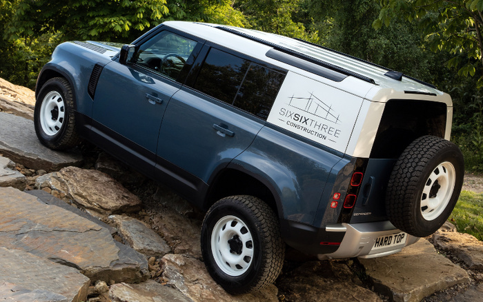 Blue and white Land Rover Defender off-roading on rocky terrain, featuring a white roof panel with 'SIXSIXTHREE CONSTRUCTION' logo and a spare tire mounted on the rear. The vehicle has white steel wheels and a rear license plate reading 'HARD TOP'. Ideal representation of rugged used cars and new cars for versatile driving conditions.