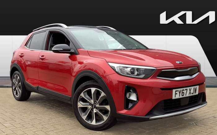 Red Kia compact SUV parked on a paved area in front of a black and white Kia dealership background featuring the Kia logo. The car has a UK registration plate FY67 XJW, alloy wheels, black trim around the wheel arches, and a silver roof rail. This image is suitable for promoting used cars and new cars.