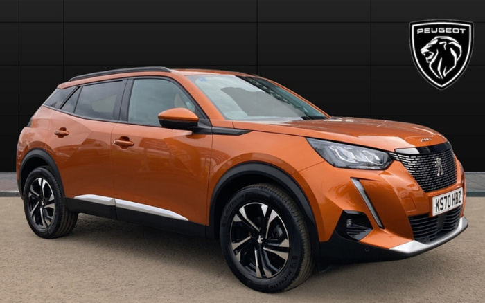 Orange Peugeot SUV parked on a grey surface against a black wall backdrop with the Peugeot lion logo displayed in the top right corner. The car has a UK registration plate reading KS70 HBZ and features sleek modern headlights, black alloy wheels with silver accents, and black trim around the windows and bottom edges. This image represents both used cars and new cars from Peugeot.