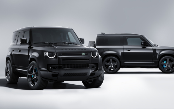 Two black Land Rover Defender SUVs displayed in a studio setting, showcasing their modern design and rugged features. The vehicles are positioned side by side, with the one in front facing slightly forward and the other viewed from the side. Perfect example of new cars and used cars available for sale.