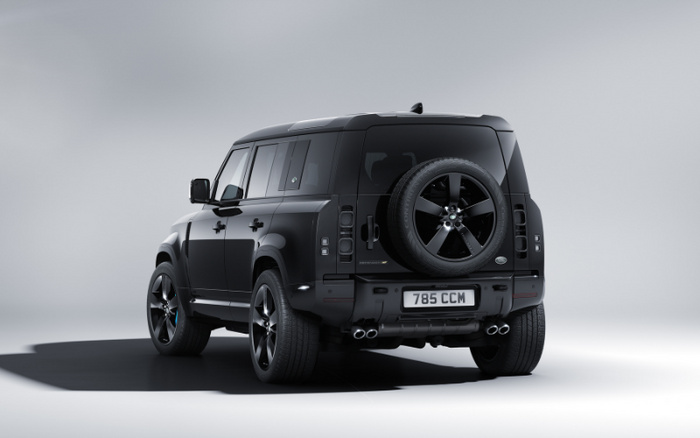 Black Land Rover Defender 110 seen from the rear and side angle in a studio setting with UK registration plate 785 CCM, featuring a spare wheel mounted on the back door, black alloy wheels, dark tinted windows, and dual exhaust pipes. Ideal image representing used cars or new cars for sale.