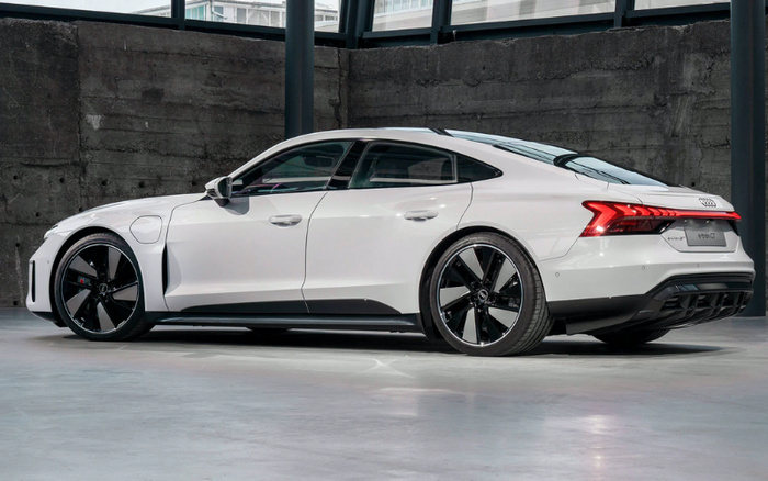 White Audi e-tron GT electric car parked indoors against a concrete wall, showcasing sleek design and black alloy wheels, ideal representation of new cars and used cars available for sale.