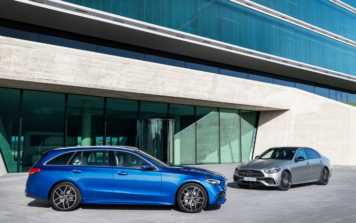 Blue Mercedes-Benz estate car and silver Mercedes-Benz sedan parked outside a modern glass and concrete building, showcasing sleek and stylish new cars ideal for buyers looking for used cars or new cars options.