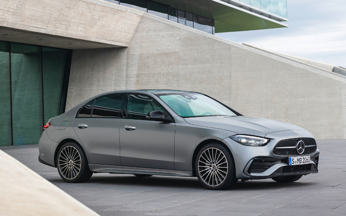 Matte grey Mercedes-Benz luxury sedan parked in front of a modern concrete building, highlighting sleek design and alloy wheels, representing new cars with potential appeal for used cars market buyers.