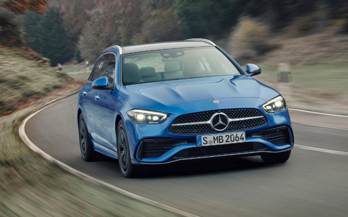 Blue Mercedes-Benz C-Class estate car driving on a curved road surrounded by trees and grass, daytime, license plate reading S MB 2064, representing stylish new cars and quality used cars.