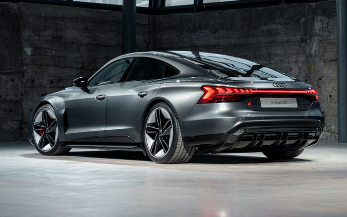 Sleek grey Audi e-tron GT electric car parked indoors against a concrete wall, showcasing distinctive rear LED lights, aerodynamic design, and stylish alloy wheels, representing a premium new car option in the market for buyers interested in used cars or new cars.