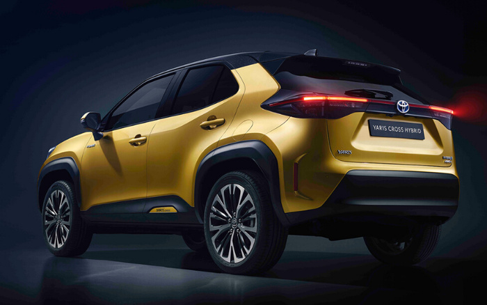 Rear-side view of a gold and black Toyota Yaris Cross Hybrid car with modern taillights illuminated, showcasing the model name 'Yaris Cross Hybrid' on the rear and 'Yaris Cross' badge on the side, representing new cars available alongside used cars options.