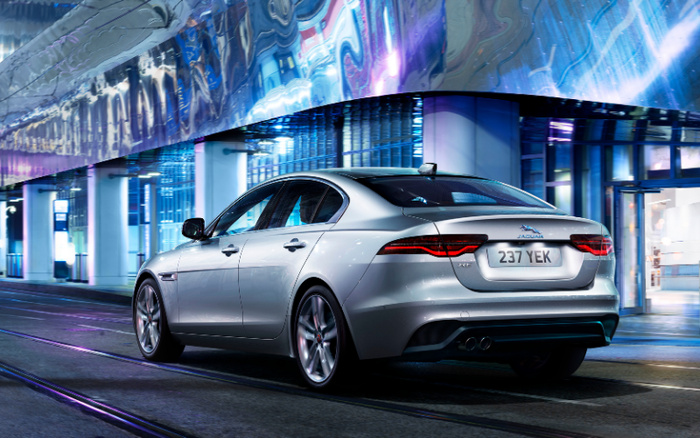 Silver Jaguar XE parked under modern reflective urban architecture at night with license plate 237 YEK, showcasing sleek design and luxury, suitable for advertising used cars and new cars in a city setting