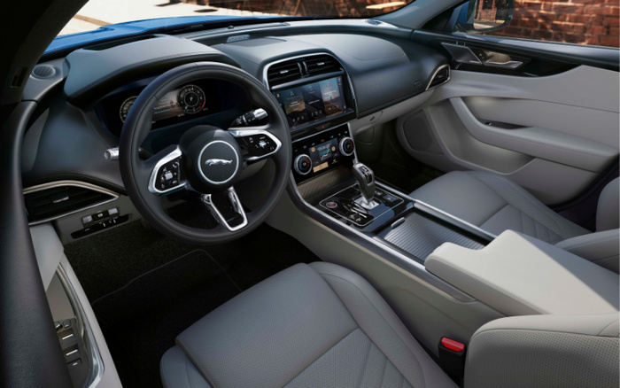 Interior view of a modern Jaguar car showcasing the steering wheel with Jaguar logo, digital instrument cluster, touchscreen infotainment system, dual climate control knobs, and leather seats. Perfect example for used cars and new cars with luxury features and contemporary design.
