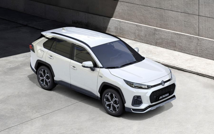 White Suzuki Across SUV parked on a concrete surface near a textured grey wall, showcasing sleek modern design with tinted windows and alloy wheels, suitable for both used cars and new cars buyers.
