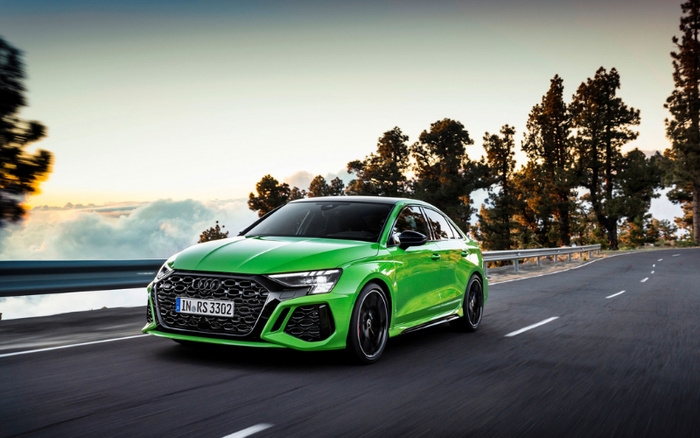 Bright green Audi RS 3 sportback driving on a winding road with trees in the background during sunset, showcasing the sleek design and sporty features of this new car model, relevant for used cars and new cars buyers.