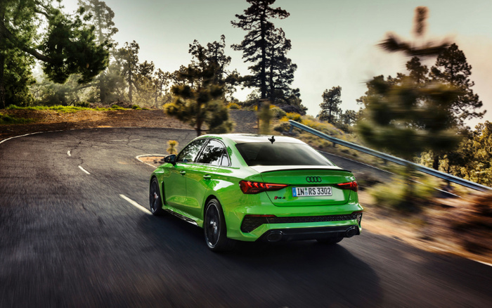 Green Audi RS3 car driving on a winding mountain road surrounded by trees in daylight. The car's rear licence plate reads IN RS 3302. The scene highlights a sporty, new car model, perfect for buyers interested in new cars or used cars.