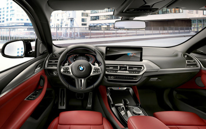Interior view of a BMW car featuring a steering wheel with the BMW logo, digital instrument cluster, central touchscreen display showing a navigation interface, red leather upholstery on the seats and door panels, and modern dashboard controls. The image highlights the luxury and advanced technology inside the vehicle, suitable for promoting used cars and new cars.