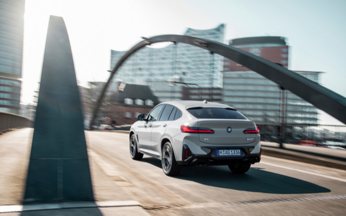 Silver BMW X4 M40i driving on a city bridge with modern buildings in the background, representing new cars and used cars in an urban environment