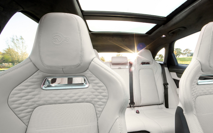 Interior view of a luxury car featuring white perforated leather seats with detailed stitching and an embossed SVR logo on the front headrests. The car has a panoramic sunroof letting in sunlight, and the back seats are visible with seat belts and headrests. The image highlights premium upholstery and spacious seating, suitable for showcasing used cars or new cars.