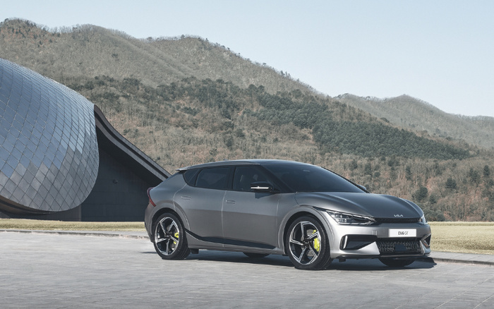 Grey Kia EV6 GT electric car parked on a paved surface with a modern architectural building and wooded hills in the background, showcasing a sleek new car model suitable for buyers interested in used cars and new cars.