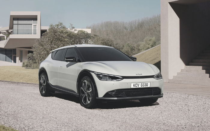 White Kia electric car parked on a gravel driveway in front of a modern house with large windows and concrete steps, showing the vehicle's front and side with license plate KCV 033G, suitable for buyers seeking used cars or new cars.