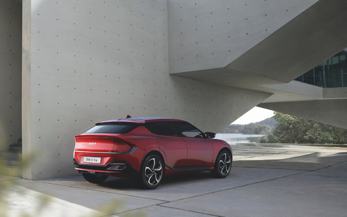 Red Kia EV6 GT-line electric SUV parked under a modern concrete structure near a waterfront, showcasing sleek rear design and black alloy wheels, suitable for buyers interested in new cars and used cars.