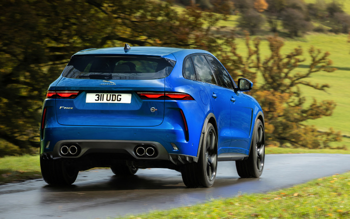 Blue Jaguar F-PACE SUV driving on a wet country road with green trees and grass in the background, featuring a rear view with the registration plate 311 UDG, dual exhaust pipes, and sleek modern tail lights, representing both used cars and new cars.