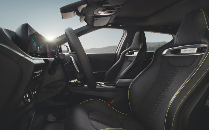 Interior view of a modern car highlighting the driver's seat and dashboard with digital displays. The seats are black with green stitching and a silver trim labelled 'GT' on the headrest. The image showcases the steering wheel, central console, and door panel with sunlight streaming through the window, emphasizing the sleek and sporty design, suitable for both used cars and new cars.