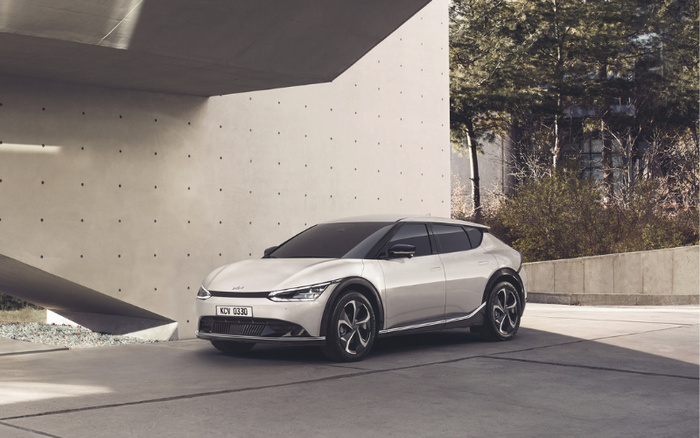 Silver Kia EV6 electric vehicle parked in front of a modern concrete building with minimalist architecture and trees in the background, showcasing sleek design and futuristic alloy wheels, suitable for advertising used cars and new cars.