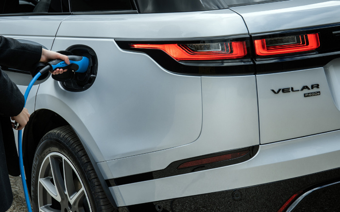 Close-up of a silver Range Rover Velar P400e electric plug-in hybrid vehicle being charged, showing a hand holding a blue charging cable plugged into the car's charging port, highlighting new cars with electric technology, suitable for used cars or new cars advertisement.