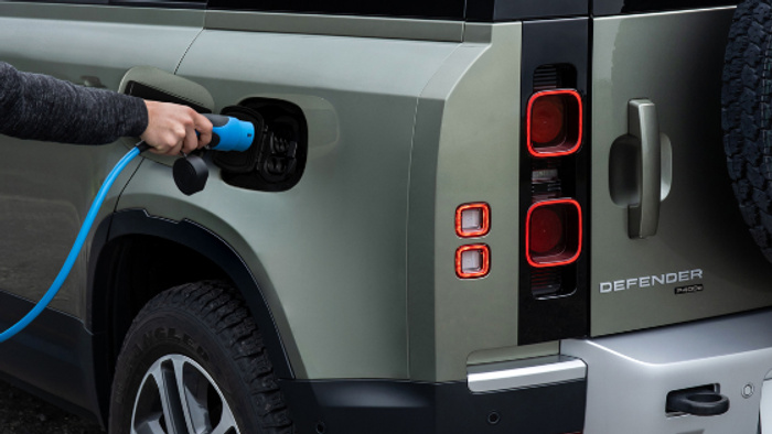 Close-up of a green Land Rover Defender P400 electric vehicle being charged with a blue electric charging cable, showing the rear light and charging port. Suitable for used cars and new cars categories focused on electric and hybrid models.