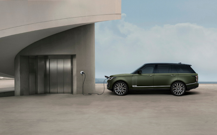 Green luxury SUV parked beside a modern concrete structure, connected to a charging station, electric vehicle charging in progress under a partly cloudy sky, suitable for used cars and new cars market.