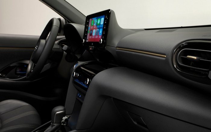 Interior of a modern car showcasing the dashboard and centre console with a touchscreen display showing app icons including phone, music, and maps. The image highlights the sleek design, textured black dashboard, steering wheel, and air vents. This interior view is representative of new cars and used cars available for sale.