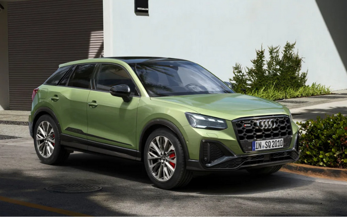 Green Audi SQ2 SUV parked outside a modern building with greenery in the background, featuring front licence plate IN SQ 2010, highlighting new cars and used cars options.