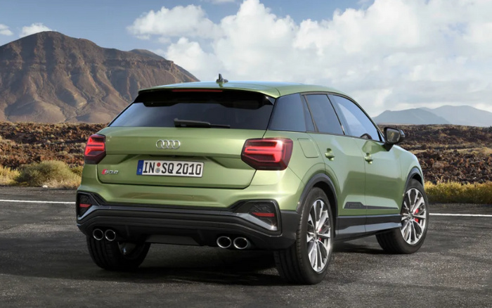 Rear view of a light green Audi SQ2 parked on a paved road with mountainous terrain and a partly cloudy sky in the background, showcasing the car's sporty rear design, quad exhaust pipes, tinted rear windows, and German license plate reading IN SQ 2010, highlighting a new car model suitable for buyers interested in used cars and new cars.