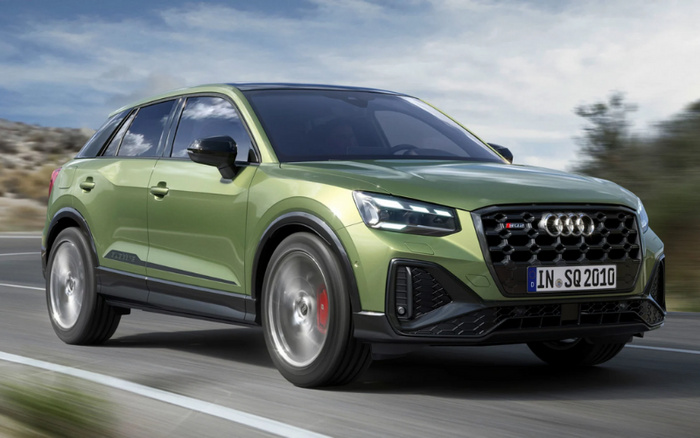 Green Audi SQ2 quattro compact SUV driving on a road under a cloudy sky, showcasing sporty design with black honeycomb grille, LED headlights, and prominent Audi logo, ideal for used cars or new cars buyers looking for luxury and performance.