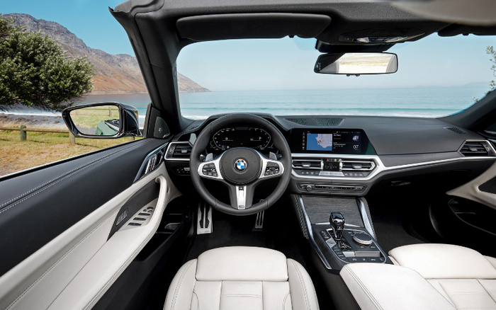 Interior view of a modern BMW car featuring a sleek dashboard, leather seats, digital instrument cluster, and central infotainment screen displaying navigation. The steering wheel bears the BMW logo. The car is parked with a scenic coastal landscape visible through the windshield, highlighting the comfort and technology suitable for buyers interested in used cars or new cars.