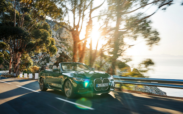 Green BMW convertible driving along a coastal road with sun shining through trees and cliffs in the background, showcasing a new car model ideal for buyers interested in new cars and used cars.
