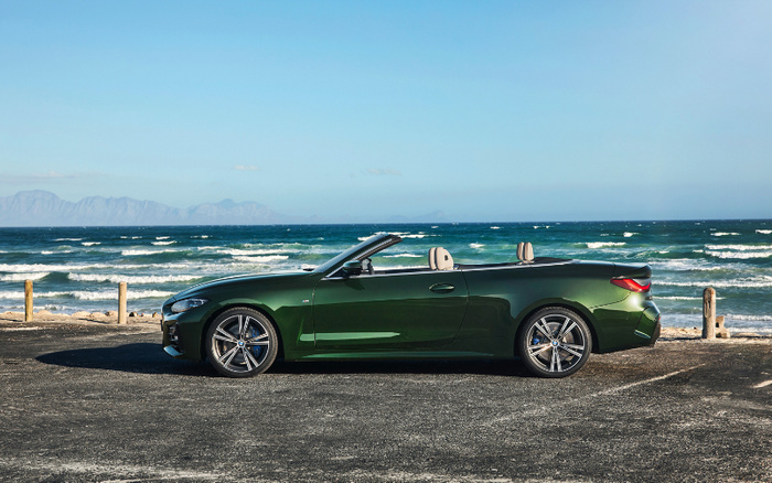 Dark green convertible car with beige interior parked by the seaside on a sunny day, with waves and mountains in the background, ideal for showcasing used cars and new cars by the beach.