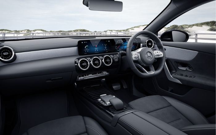 Interior of a modern Mercedes-Benz car showcasing the dashboard with a wide digital display featuring navigation, vehicle information, and music controls. The steering wheel has the Mercedes logo with multiple control buttons, surrounded by sleek black and silver trims. The cabin highlights black leather seats and detailed stitching, with circular air vents and a minimalist centre console. This stylish interior represents the quality found in both used cars and new cars.