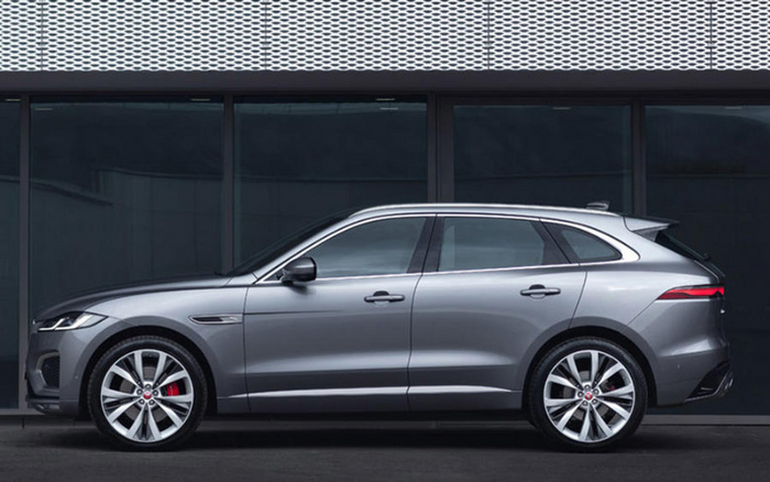 Side view of a sleek silver luxury SUV parked in front of a modern dark glass building with a silver perforated metal panel above. Suitable for used cars and new cars listings.