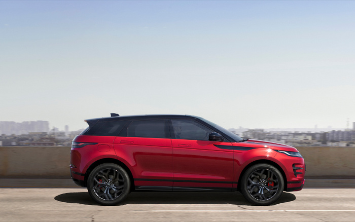 Red new car driving on a road with cityscape in the background, showcasing sleek aerodynamic design and black alloy wheels, suitable for advertising used cars and new cars.