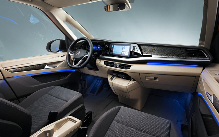 Interior view of a modern Volkswagen car showing the driver's seat, steering wheel with VW logo, digital dashboard, and central touchscreen displaying navigation. The cabin features black and beige upholstery with blue ambient lighting along the dashboard and doors. The clean and spacious layout highlights the car's contemporary design, ideal for buyers interested in used cars or new cars.
