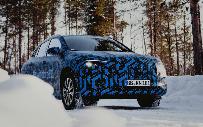 Front view of a camouflaged blue and black patterned car driving on a snowy road surrounded by trees, with headlights on and a visible German license plate reading BB RN 101. The side of the vehicle displays the text #switchtoEQ, suggesting an electric or new car model, making it relevant for used cars and new cars search keywords.