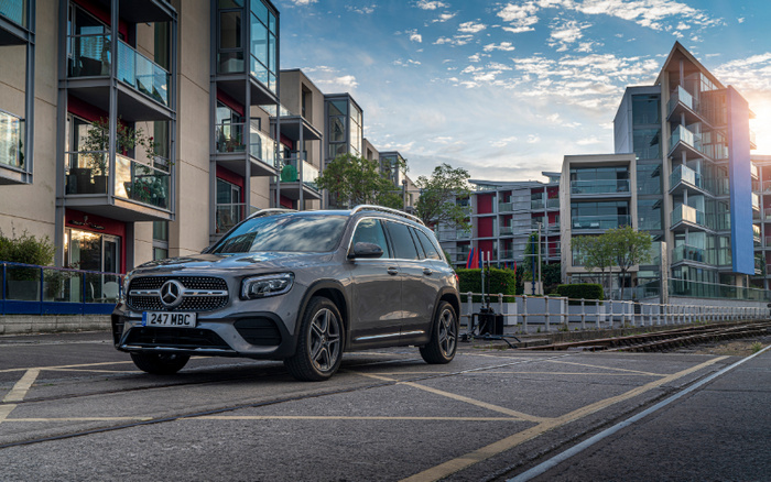 Silver Mercedes-Benz SUV parked on a street beside modern apartment buildings under a partly cloudy sky, featuring a license plate reading '247 MBC'. The setting highlights used cars and new cars in an urban environment.