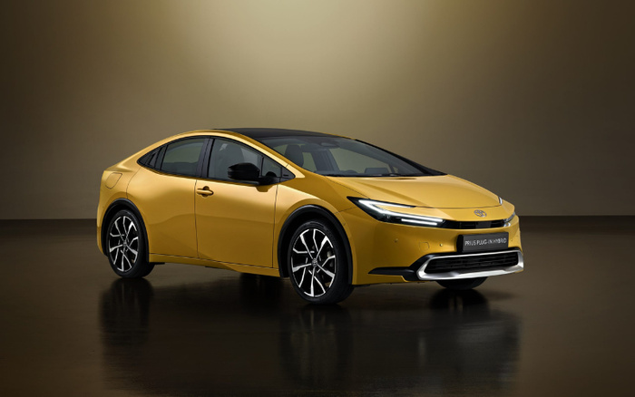 Sleek yellow Toyota Prius Plug-in Hybrid new car displayed in a studio with a reflective black floor and plain dark background, showcasing modern design with sharp LED headlights and black alloy wheels, ideal for buyers interested in used cars or new cars.