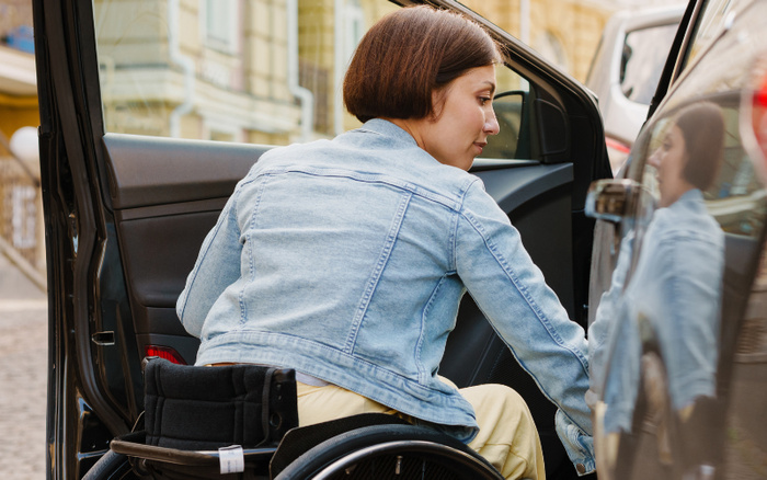Woman in a wheelchair opening the door of a car, demonstrating accessibility and ease of use for used cars and new cars, highlighting inclusive vehicle options in an urban setting.